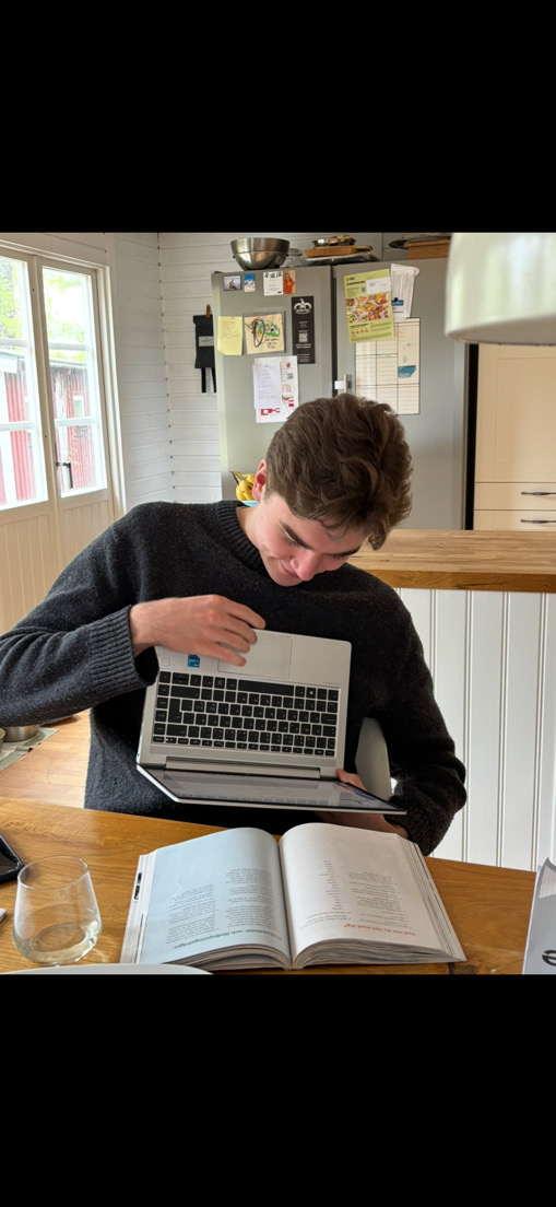Tom sitter vid ett köksbord och pluggar med laptop och en uppslagen bok